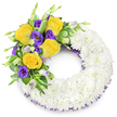 A carefully composed circular funeral wreath set against a clean white background, its form crafted from a dense, cloud-like ring of small, pristine white spray chrysanthemums. The chrysanthemums are tightly clustered so their many layered petals read as a soft, velvety surface - cool, muted and reverent - the kind of texture you might want to rest a hand on. Nestled into the upper-left quadrant is a bright, reassuring spray of colour: several fully opened yellow roses, their buttery petals unfurling with a faint, warm tea-rose scent, paired with rich, velvety purple lisianthus (Eustoma) whose ruffled cups lend depth and a quiet dignity. A few pale-lavender lisianthus buds and slender green shoots peek from the cluster, suggesting gentle movement and natural growth. Various glossy green foliage - rounded salal-like leaves, lightly variegated foliage and delicate fern fronds - frames the blooms and gives structural contrast, allowing the yellow and purple to sing against the white chrysanthemum field. Subtle dark purple mesh ribbon is visible beneath the flowers at the inner and outer rims of the wreath, a delicate echo of the lisianthus tones that ties the composition together. The overall impression is serene, respectful and handcrafted, an arrangement suited for memorials or funeral services in and around Stanmore - perhaps for a chapel on Stanmore High Street or a quiet service near Bentley Priory. As a local florist's description, it honours purity and remembrance while offering a tactile, comforting presence for bereaved families.