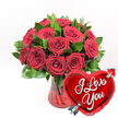 This image showcases a classic romantic gift: a sumptuous bouquet of deep crimson roses arranged in a ruby-red glass vase, accompanied by a bright red heart-shaped balloon, all set against a pure white background. The bouquet features around a dozen or more roses, gathered closely to form a generous, dome-like shape at the top of the vase. Each rose displays lush, velvety petals in a rich, dark red tone, some flowers fully open in wide spirals, others only partially unfurled, lending the arrangement a sense of natural progression and life. Between and around the blooms, vibrant green foliage adds fresh contrast, the leaves smooth and glossy, framing the roses with a crisp, clean edge. The vase itself is clear glass infused with a ruby tint, its fluted sides gently ridged, catching the light in soft reflections that lend a subtle sparkle, similar to sunlight on the windows of Stanmore's high street shops. Through the glass, the stems are visible where they cross and angle into the water, hinting at the careful structure beneath the opulent top. In the lower right foreground, partly overlapping the base of the bouquet, stands a radiant heart-shaped foil balloon. It is a vivid, metallic red, polished to a mirrorlike finish, and bears the phrase I Love You in bold white cursive script across the centre. A sleek silver Cupid's arrow seems to pierce the heart on a diagonal from bottom left to upper right, symbolising love that has found its target. Together, the roses and balloon create a timeless expression of affection, ideal for Valentine's Day, anniversaries, or surprise romantic deliveries to homes across Stanmore and the surrounding area.