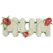 A dignified three-dimensional tribute reads MOM in large, freestanding letters made entirely from hundreds of small, pristine white spray chrysanthemums. Each bloom is chosen for fullness and pure colour, packed tightly to form a soft, cushion-like surface that looks almost clouded in gentle daylight. The white texture suggests quiet peace and simple dignity; the faint, fresh scent of chrysanthemums and verdant stems lingers like a memory. Against the white, three deep red blooms-glossy anthuriums with their smooth, heart-shaped spathes and pale yellow spadices-are placed with considered grace: one at the upper left of the first M, a second nestled at the base of the central O, and a third mirrored on the upper right of the final M. Clusters of feathery fern and broader dark green leaves cradle each red focal point, their matte greens softening the arrangement's edges and adding a woodland depth. A subtle dark green structural frame peeks out between blooms, giving the letters a clean outline and freestanding stability without detracting from the flowers' gentleness. Long, arching blades of grass and slender stems sweep lightly across the white letters, visually connecting the red anthuriums and guiding the eye across the tribute. Bathed in soft morning light, this arrangement radiates calm reflection and enduring love-suitable for a funeral service, wake, or graveside memorial where family members in Stanmore and nearby Harrow seek a simple, heartfelt expression of remembrance for a mother.
