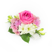On a crisp white backdrop a compact, hand-crafted corsage sits like a small promise of celebration: a lush bubblegum-fuchsia rose takes centre, its velvet petals tightly wound at the heart and unfurling outward in soft, concentric layers. Around it, clusters of pastel pink and lavender hydrangea form a pillowy halo, each tiny floret adding airy volume and a whisper of spring. Interspersed are creamy white, trumpet-shaped blooms-suggestive of small alstroemeria or miniature lilies-with faint green throats that catch the light and lend a note of pure freshness. Glossy, deep green leaves peek from beneath the blooms, their broad surfaces grounding the arrangement and giving it a cool, verdant base. Slender, upward-sweeping green buds, tipped faintly with yellow, introduce energetic movement and the sense that more blooms will open in time. At the bottom right a delicate cluster of luminous white pearls is tucked among the flowers, their satin sheen playing against petals and adding an heirloom touch suited to weddings or proms. Soft, natural illumination sculpts each curve and shadow so the textures-velvet rose, feather-light hydrangea, satiny pearls-are almost tangible, and the scent feels quietly floral and clean. This intimate design evokes bridal details, corsages, and understated formal accessories, ideal for spring and early-summer ceremonies, anniversaries, or garden parties in Stanmore and nearby Canons Park, offering a graceful, tactile statement of love and refinement.