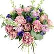 Captured against a clean white background, this bouquet feels like an intimate moment of beauty, the kind a Stanmore florist might create for a quiet celebration at home on a leafy side street. At its core, large garden roses in soft blush, dusty pink, and gentle mauve open fully, each bloom revealing a swirl of velvety petals that evoke classic romance and warmth. Nestled around them, ruffled carnations provide generous fullness, their petals layered and slightly curled, fading from creamy, almost vanilla centres to blush and deeper rose along the fringes, giving the bouquet a billowing, textured appearance. Cutting through the softness, deep indigo and royal blue flowers introduce a vivid, jewel-like contrast: some remain as elegant, tulip-shaped buds, while a single open blue anemone near the front stands out with its rich colour and dark, nearly black centre, like a tiny night sky among pastels. Slender stems of pale lavender and lilac stock flowers weave upward through the bouquet, each dotted with small blossoms that add height and an airy, almost ethereal feel, reminiscent of early spring walks near Stanmore Country Park. The flowers are surrounded by a collar of fresh greenery, including rounded, silvery eucalyptus leaves and deeper green foliage, whose different textures and tones frame the blooms and suggest a light, refreshing scent. At the base, the neatly tied stems are visible, underscoring the hand-crafted nature and freshness of the arrangement. This palette of pinks, purples, blues, and greens creates a bouquet that feels both comforting and refined-perfect for offering sympathy, celebrating an anniversary, or simply sending a gentle reminder of care to someone in Stanmore or the neighbouring areas.
