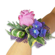 A single wrist corsage captured on a fair-skinned forearm, set diagonally against a clean white background so every hue reads with clarity and light. At its heart sits a generous, partially open rose in a soft pink that deepens to magenta at the ruffled edges, each velvety petal layered like a satin bowl and suggesting a faint, fresh-rose scent. Nestled close are clusters of saturated indigo-purple hydrangea, their tiny florets pooling together with subtle blue-tinged centres that catch the light and give an almost luminous depth. Interwoven throughout are long, silvery-green sprigs-eucalyptus or lavender-like in texture-that add a cool, dusty softness against the lush blooms. Variegated ivy frames the composition with its dark green centres and creamy, yellow-tinged margins, while a sculptural curled leaf striped in white and green creates a contemporary spiral, introducing a crisp graphic line. Underpinning the flowers is an open-weave mesh of deep violet, its lacy weave peeking out like evening shadow and amplifying the purple notes of the hydrangea. The overall touch is both fresh and composed: petals that invite a gentle press of the fingertips, glossy ivy, and the feathered breath of the silvery foliage. This piece reads as modern romance-perfect for a bridesmaid, prom guest, or anyone wanting a refined accent for a celebratory evening. I picture it worn under soft gallery light or the warm glow of a Stanmore Broadway reception, a small floral jewel that feels personal, polished, and quietly joyful.