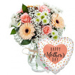 This image shows a warm and joyful Mother's Day gift combination arranged against a spotless white background, reminiscent of a bright morning in a Stanmore living room with light pouring in through large windows. The main focus is a lush, mixed bouquet displayed in a clear, lightly textured glass vase. The stems inside are visible, aligned in a tidy cluster that reflects the practiced touch of local florists at Flowers Stanmore. Around the vase's neck, a slim strand of rustic twine is tied in an easy bow, reinforcing the personal, hand-crafted feeling of the gift. The bouquet is rich with pastel tones: several peach-pink roses are in full bloom, their layered petals unfolding gracefully, each flower soft and velvety to the eye. Complementing them are generous peach gerbera daisies, their wide petals radiating out from dark brown or nearly black centres, giving the impression of small suns shining within the bouquet. Between these larger focal blooms, airy sprays of white baby's breath weave a delicate, cloud-like network, softening transitions and lending an almost whisper-light texture. Small white and pale green chrysanthemums fill out the design, their daisy-like shapes bringing brightness and resilience, much like the gardens and hedgerows around Stanmore's residential lanes. Glossy green foliage supports and frames the flowers, adding depth and vivid contrast to the softer hues. To the right of the bouquet, a heart-shaped Mylar balloon floats, visually tethered to the arrangement though its string is subtle. The balloon's smooth surface is mostly white or soft cream, scattered with metallic golden-peach and neutral dots that sparkle as they catch the light, echoing the energy of a family celebration. At the centre, a peach-toned heart shape encloses the words Happy Mother's Day in an elegant, stylised script, the letters large and flowing. A small white greeting card, partly hidden behind the vase and balloon, hints at a personal message. Together, these elements create a complete and heartfelt visual tribute to mothers, perfectly suited to a Stanmore Mother's Day delivery.